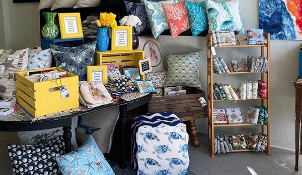 A collection of throw pillow, photo frames, vases displayed on a table and shelves.   Books displayed on  small bookshelf.