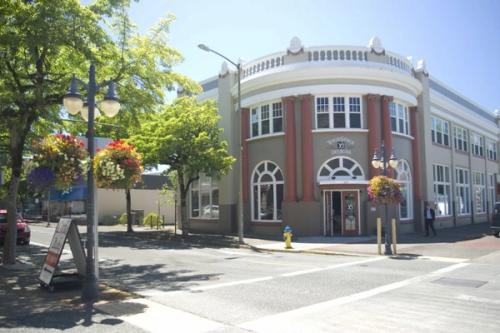 A sunny corner in historic downtown Coos Bay, featuring a curved brick commercial building adorned with hanging flower baskets and classic street lamps.