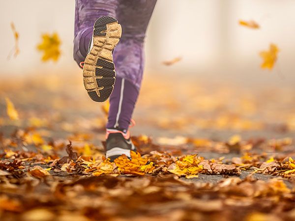 A close-up of a runner's feet mid-stride on a path covered in fallen autumn leaves, representing running on Oregon's Adventure Coast.
