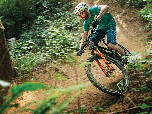 A mountain biker leans into a sharp turn on a dirt trail surrounded by lush forest at the Whiskey Run Trails near Coos Bay, Oregon.