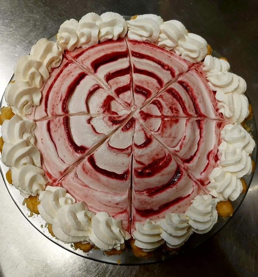A round cake with a swirl of red and white frosting, topped with piped whipped cream rosettes around the edge.