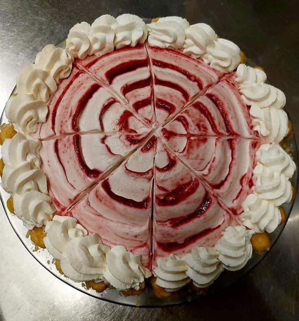 A round cake with a swirl of red and white frosting, topped with piped whipped cream rosettes around the edge.