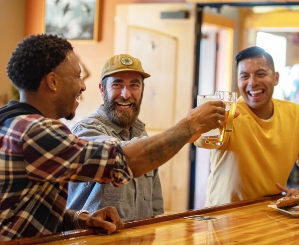 Three friends toasting with beers at the bar inside 7 Devils Brew Pub.