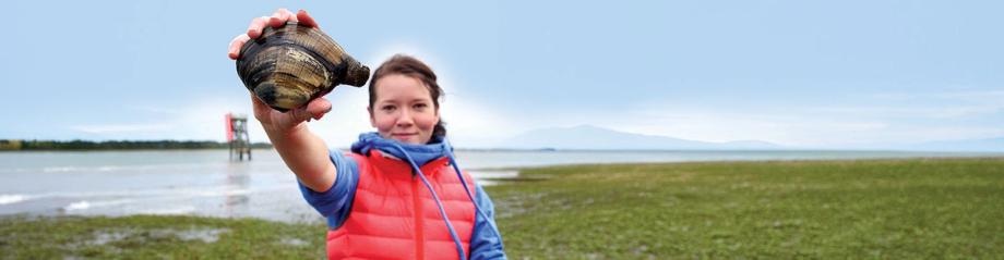 A woman holds up a large gaper clam on the tidal mud flats along Lower Coos Bay.