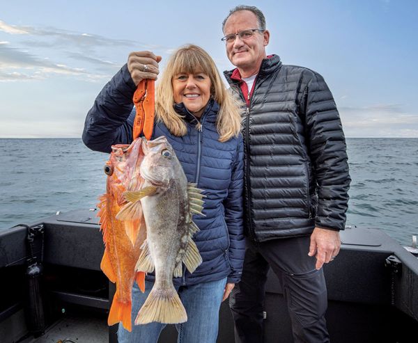 A smiling couple holds up two freshly caught rockfish aboard a charter fishing boat off the Oregon Coast, with open ocean visible in the background.