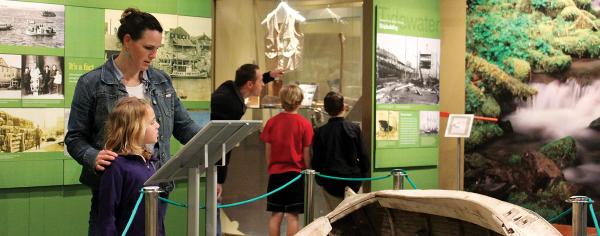 Families explore the Tidewater shipbuilding exhibit at the Coos History Museum, with a historic wooden boat hull and archival photos on display.