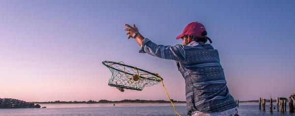 Man casting a crab ring net into the water at sunset from Hollering Place on Oregon's Adventure Coast.