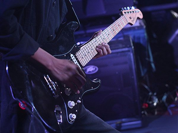 A musician plays an electric guitar under purple stage lights, representing the live entertainment, theaters, and nightlife scene.