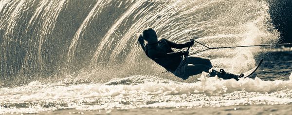 Silhouette of a water skier carving a sharp turn, throwing up a large wall of spray at sunset.