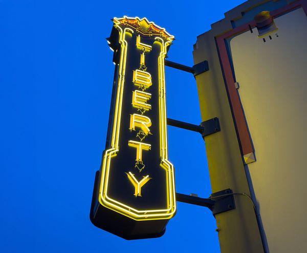 alt="The glowing yellow neon blade sign of the Liberty Theater in North Bend, photographed against a deep blue evening sky.