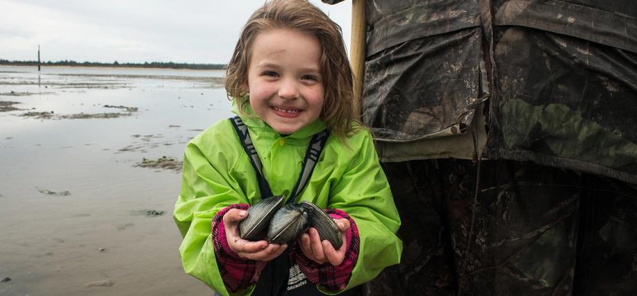 little-girl-clamming-charleston.jpg alt="A young girl smiling and holding freshly dug clams on a tidal flat in Charleston, Oregon.