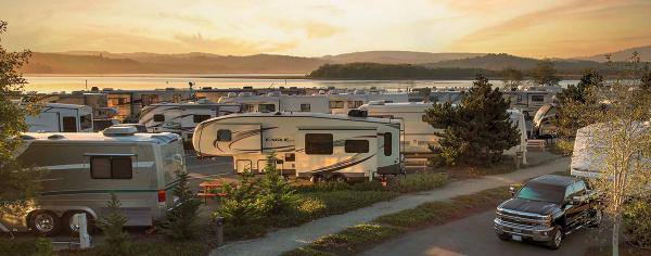 Rows of RVs fill the Ko-Kwel Casino Resort RV park near Coos Bay at sunset, with a calm bay and rolling hills in the distance.