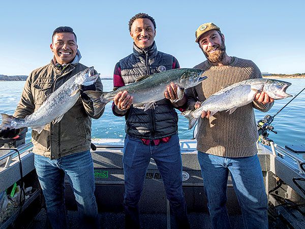 Three smiling men stand on a fishing boat, each holding a large salmon, on the Oregon Coast.