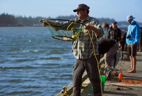 A man casting a crab ring net from a dock at Charleston Marina, with other crabbers and gear visible in the background.