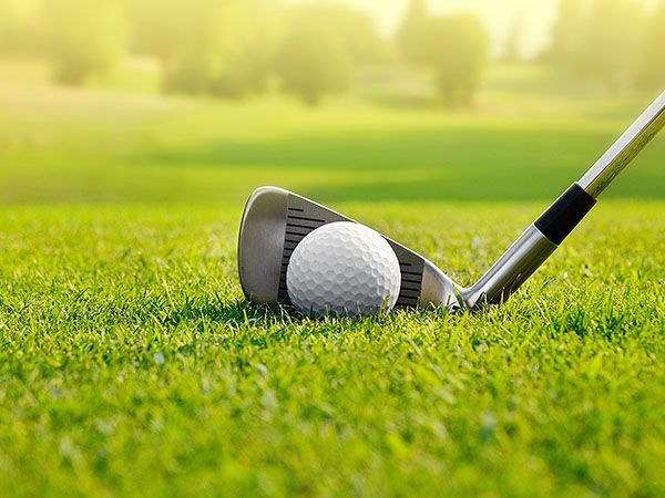 A close-up of a golf ball and iron club on a lush green fairway, representing golfing on Oregon's Adventure Coast.