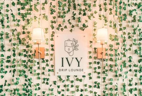 Ivy Drip Lounge sign mounted on an ivy-covered wall flanked by two brass wall sconces.