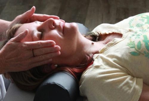A practitioner administers a Reiki energy healing session with hands gently placed on a woman's head as she rests with eyes closed.