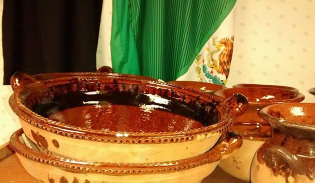 Stacked ceramic bowls and pots with brown glaze, displayed in front of patterned fabric and curtains.