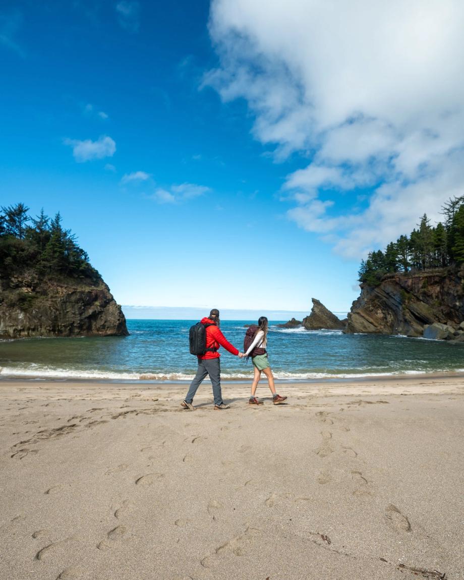 Scenic view of Simpson Beach featuring two hikers on the sand between rocky headlands along the Oregon coast.