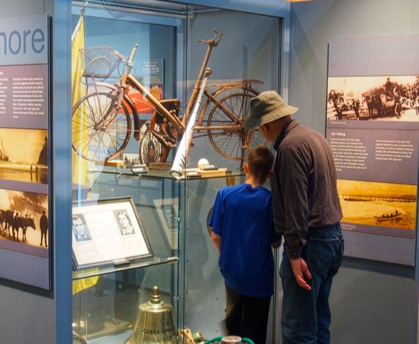 A man and boy examine a glass display case containing a vintage bicycle and historical artifacts at the Coos History Museum.