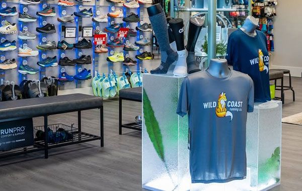 A Wild Coast Running Co. shirt display alongside shoes, socks, and gear on the walls of the running store.