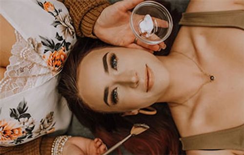 A woman reclines during a facial treatment with a skincare product held near her face.