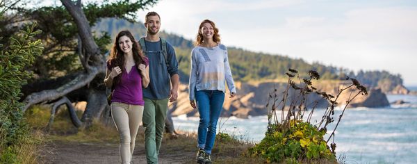 Three friends walk together along a coastal trail with rugged headlands and ocean views on the Sunset Trail.