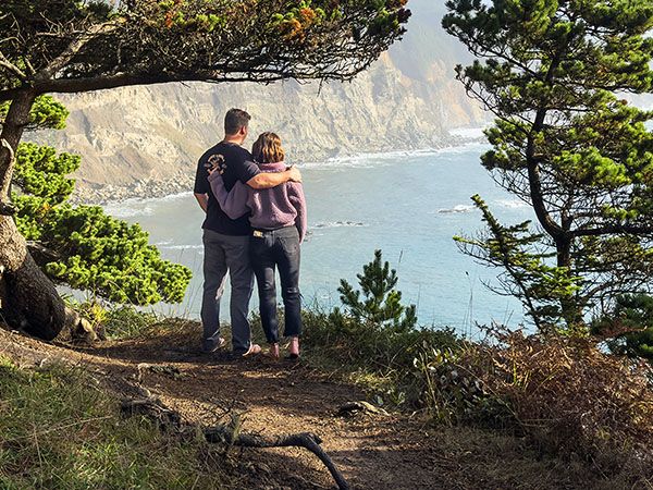 A couple stands with their arms around each other, taking in the dramatic coastal cliffs and ocean views at Cape Arago State Park on Oregon's Adventure Coast.