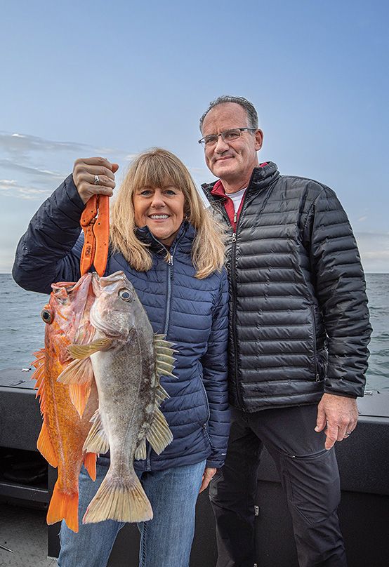 woman holding two fish with husband by her side on a boat