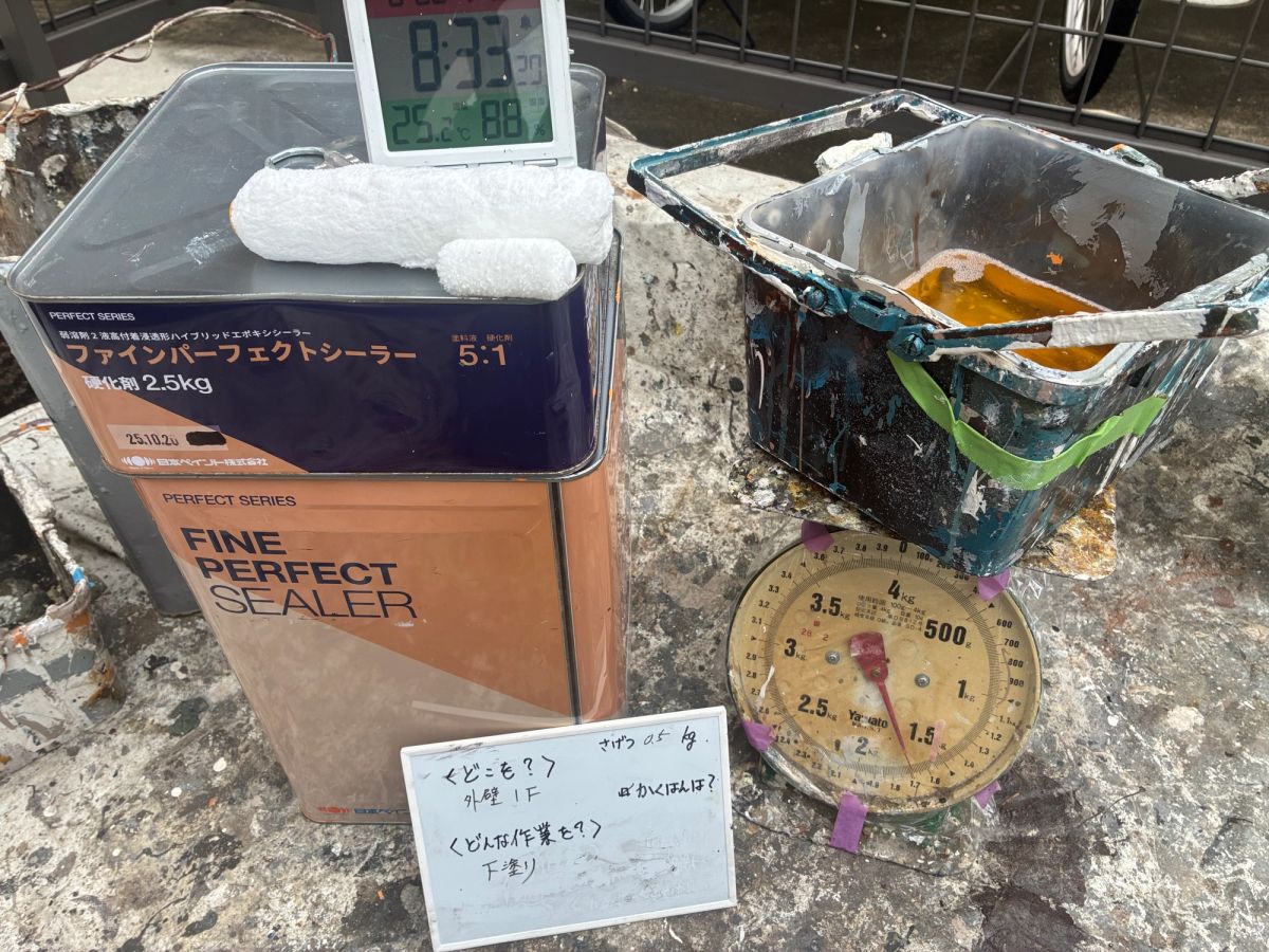 材料の缶と温湿度計、計量用のはかり、袋から出す前の新品ローラーを並べて撮った現場の記録写真。温湿度計は8時33分・気温25.2℃・湿度88%を表示している。