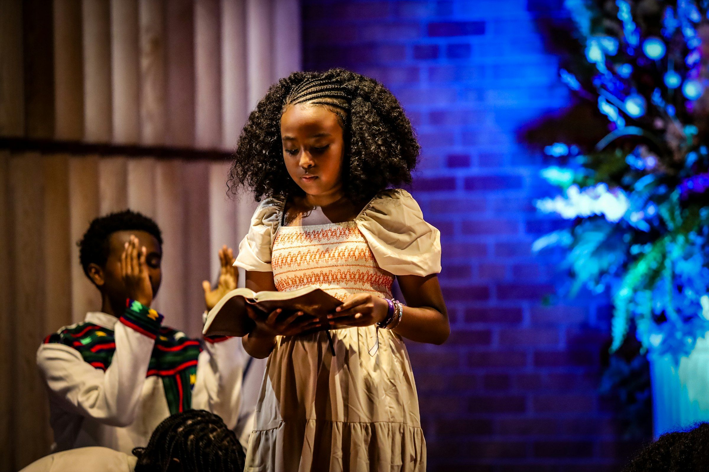 A young girl reading from a book on stage