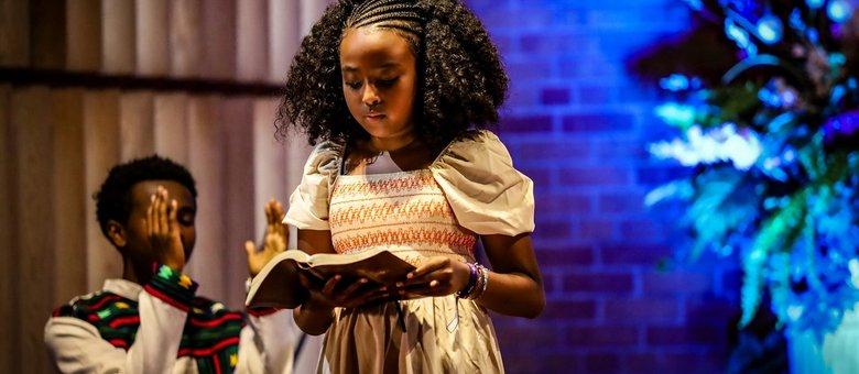 A young girl reading from a book on stage