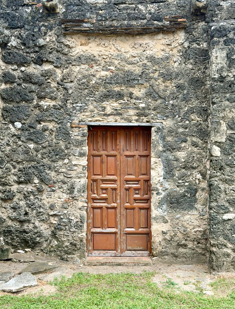 Paneled wooden double doors in a small opening surrounded by rough gray limestone at Mission Concepción.