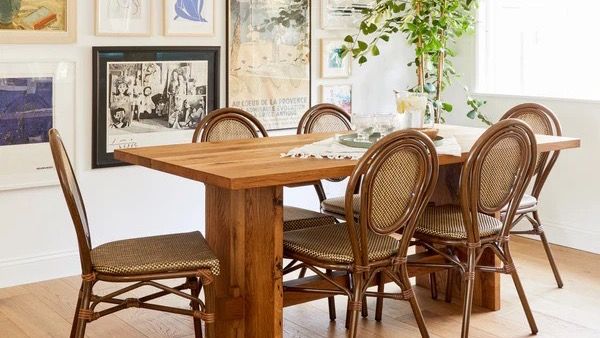 A solid oak What We Make dining table with rattan bistro chairs, in a dining room with a gallery wall