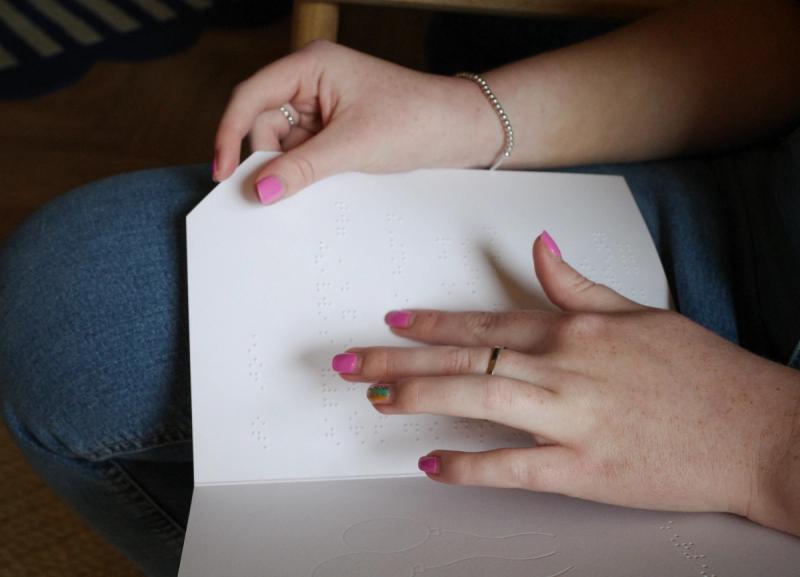 A braille printed card being read in someone's lap using their hands