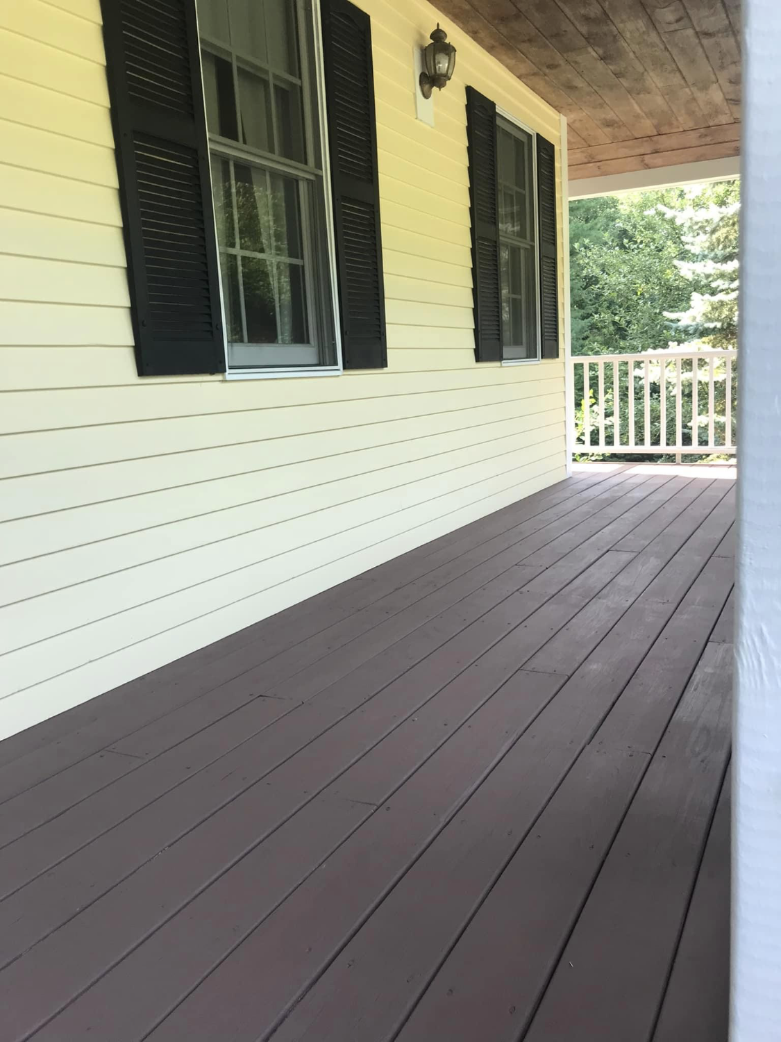 A dark-stained porch floor against yellow siding and white trim painted by Brookstone Painting and Carpentry in Plymouth County and Cape Cod