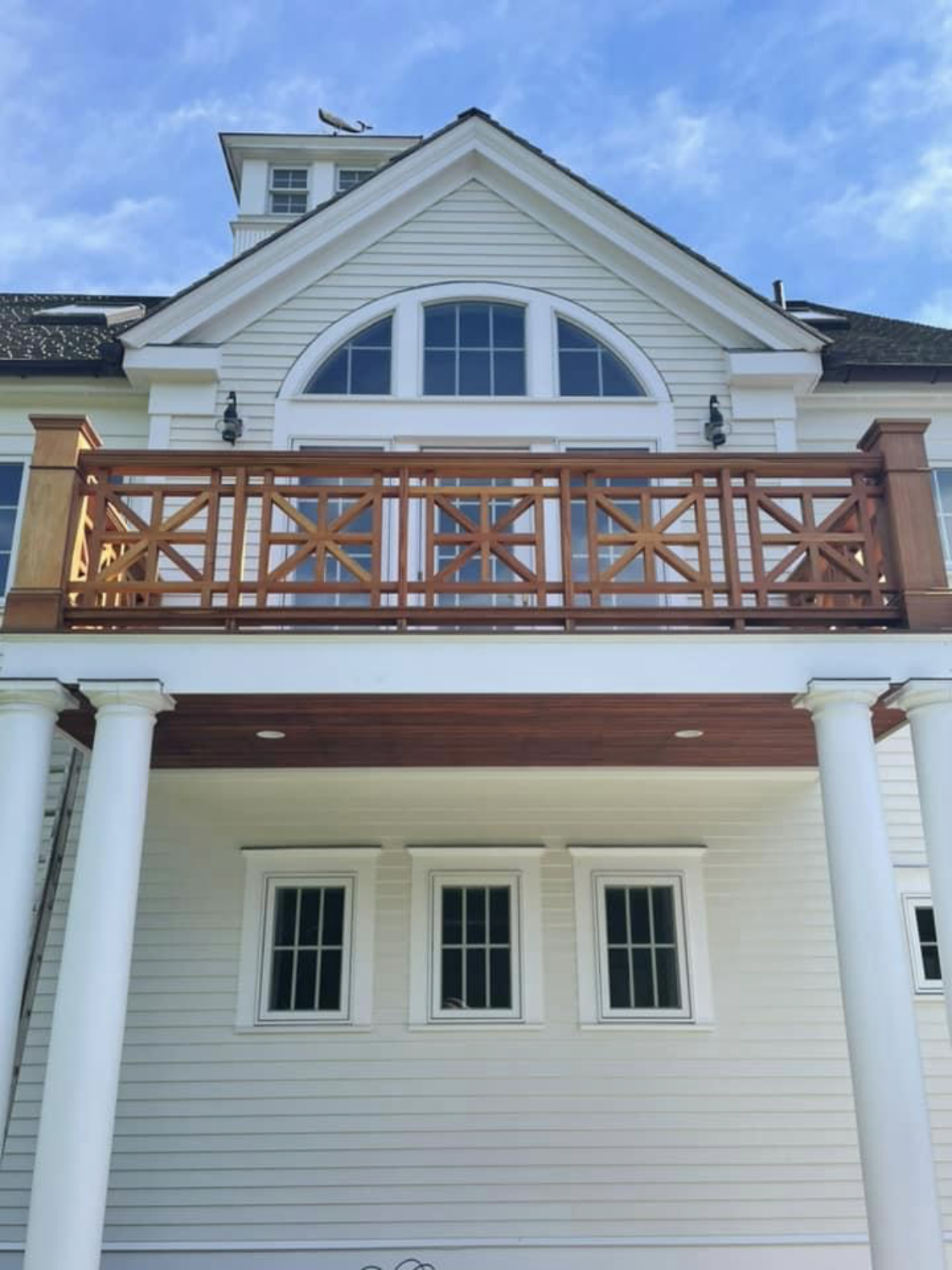 A white home with fresh siding and a wood balcony painted by Brookstone Painting and Carpentry in Plymouth County and Cape Cod