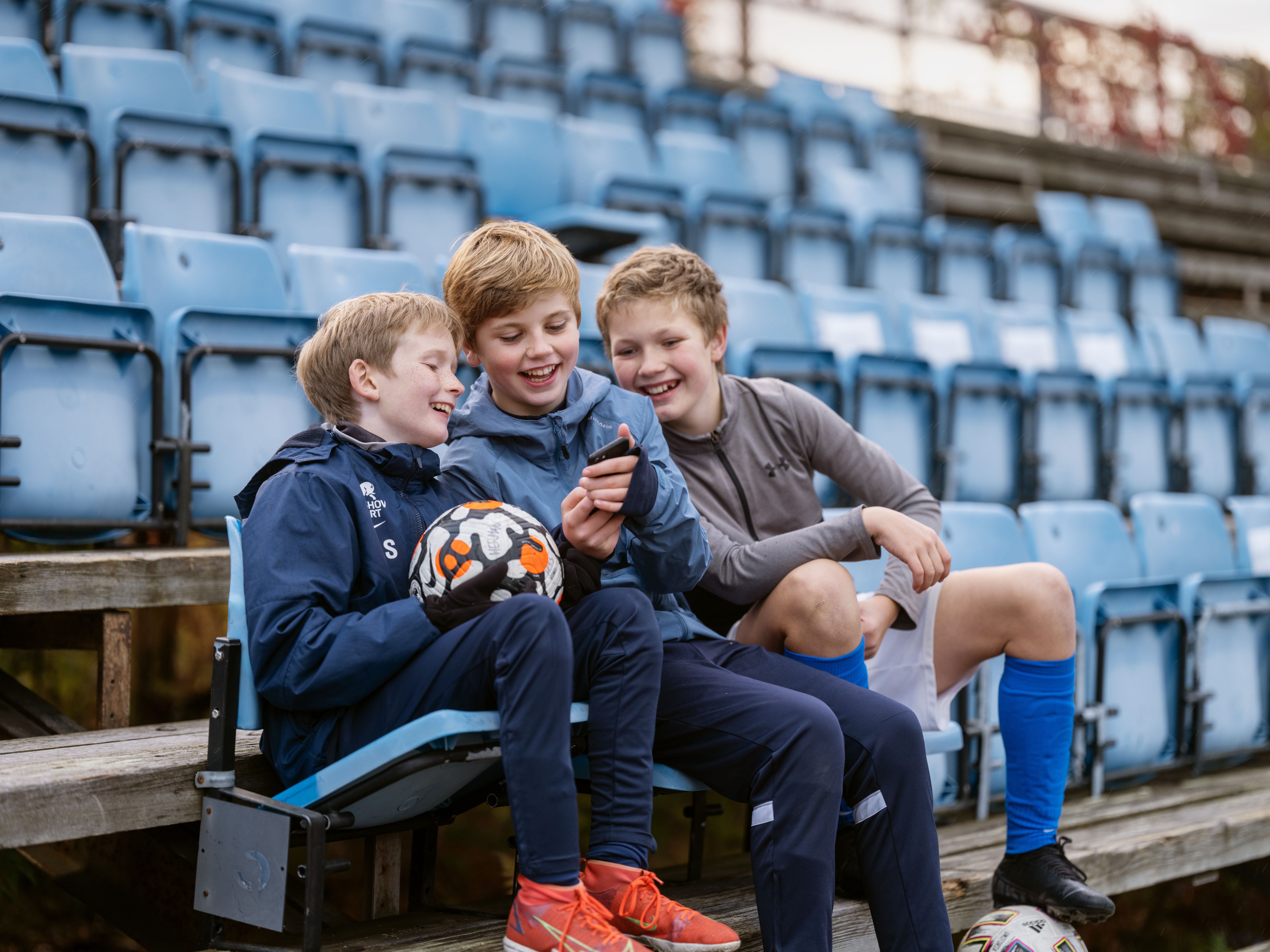 Tre gutter på fotballtrening som ser på telefon i hånda. Foto. Kreditering: Spleis