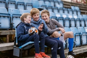 Tre gutter på fotballtrening som ser på telefon i hånda. Foto. Kreditering: Spleis