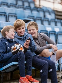 Tre gutter på fotballtrening som ser på telefon i hånda. Foto. Kreditering: Spleis