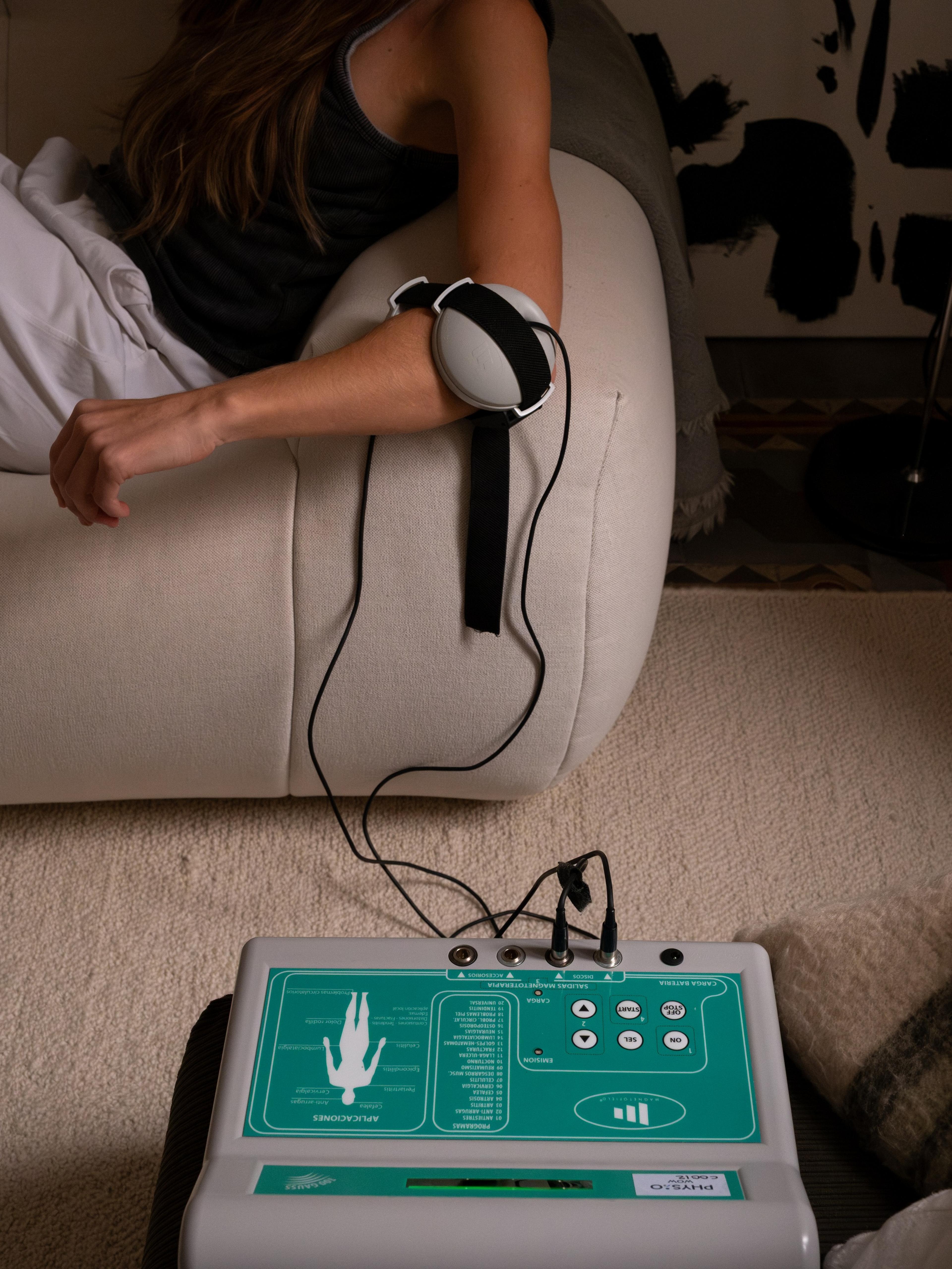 Persona con un aplicador de magnetoterapia colocado en el brazo, junto al panel de control del aparato