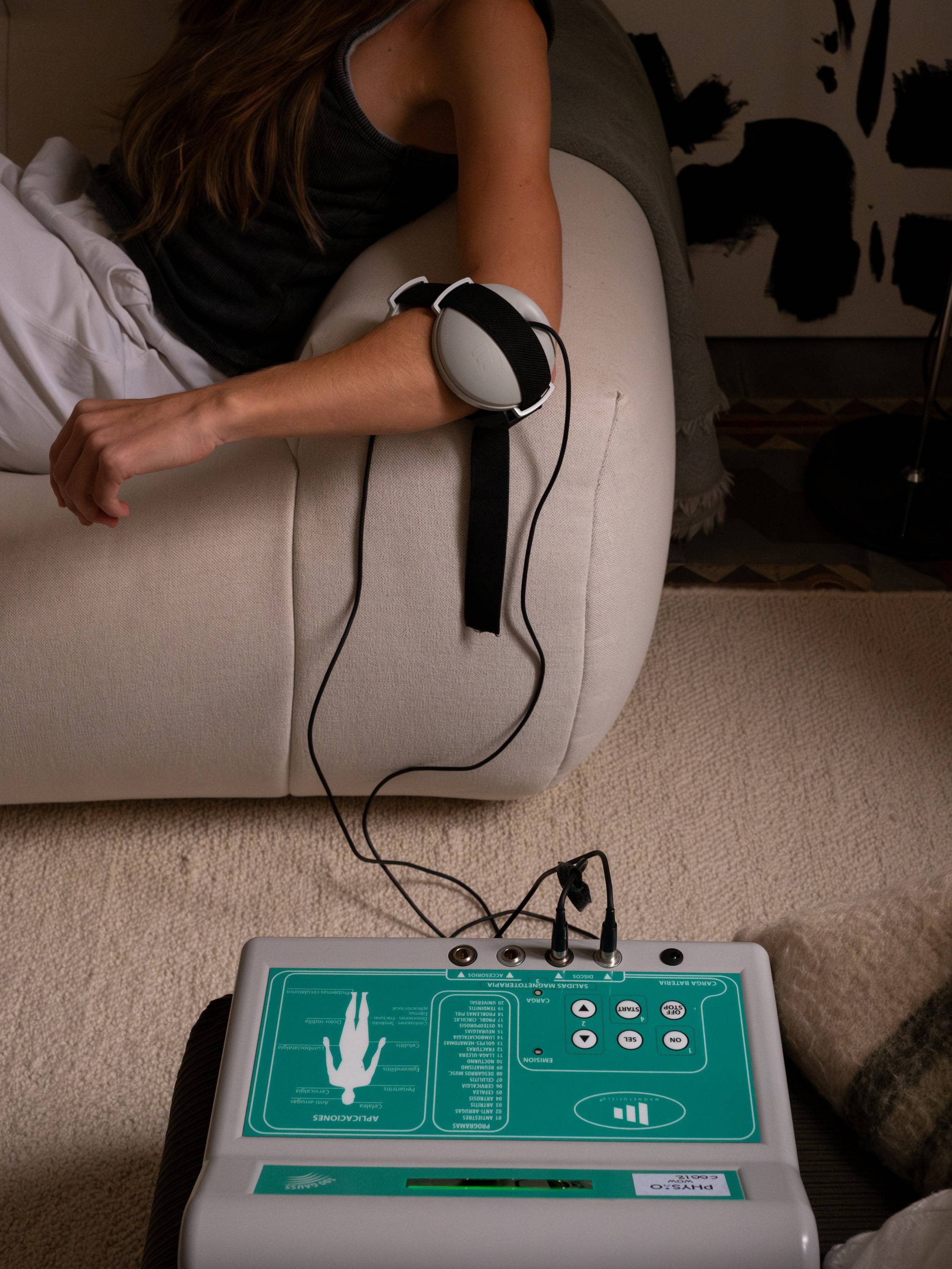 Persona con un aplicador de magnetoterapia colocado en el brazo, junto al panel de control del aparato