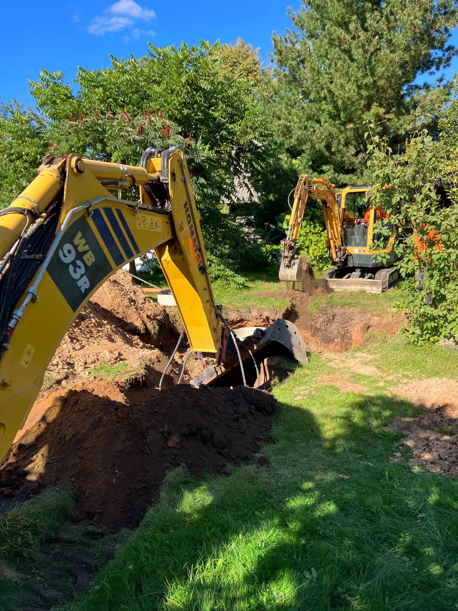 Komatsu WB93R ir mini ekskavatorius kasa tranšėją komunikacijoms sklype