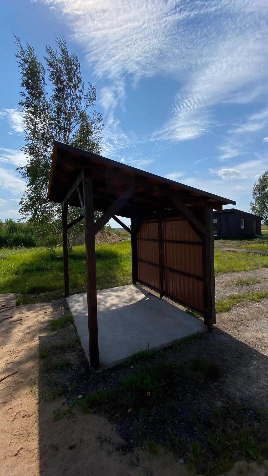 Nedidelė medinė pavėsinė tamsiu stogu ant betoninio pagrindo