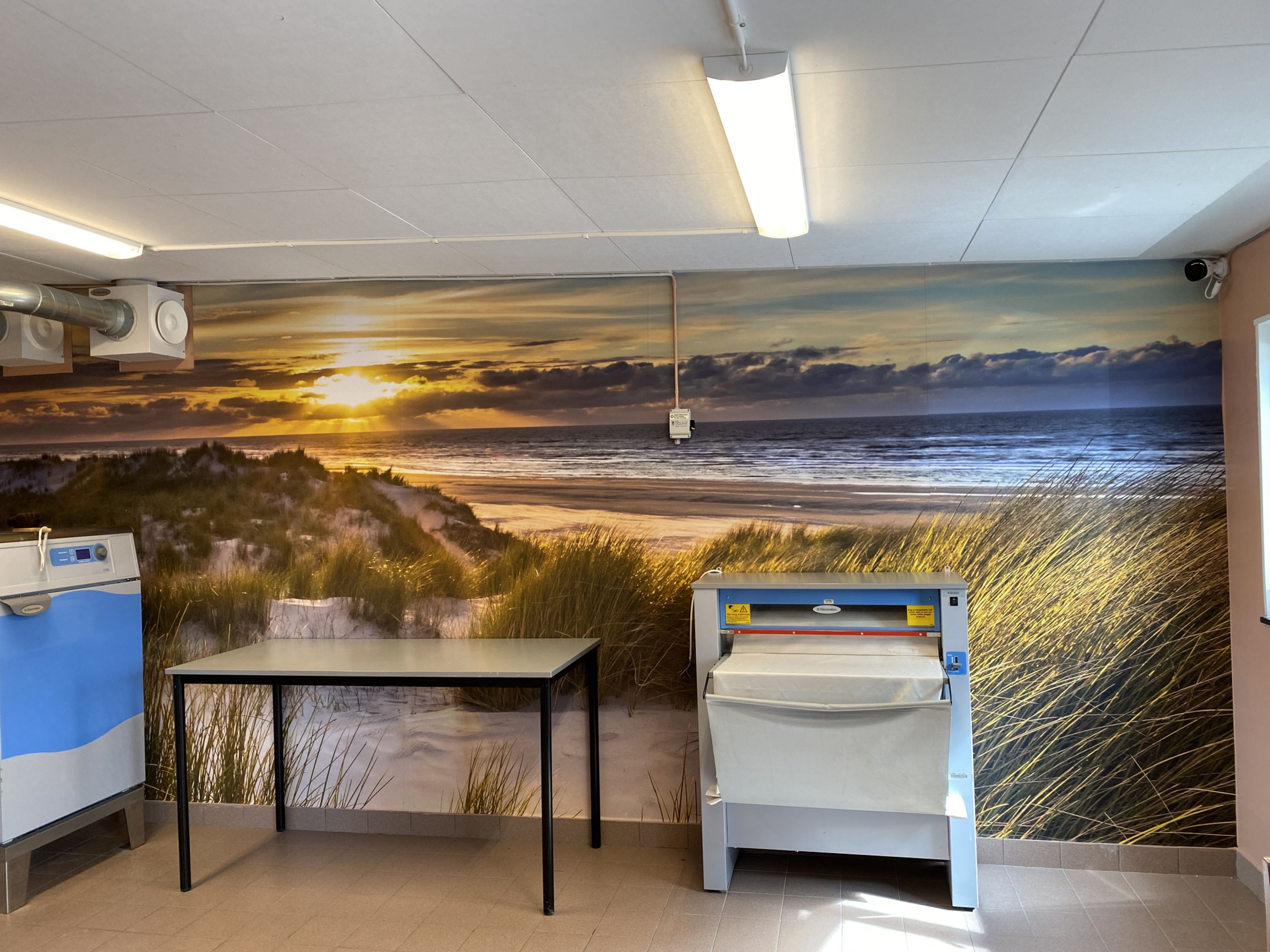 Visar tapeten som sattes upp i tvättstugan som visar hav, strand, sol och vatten. 
