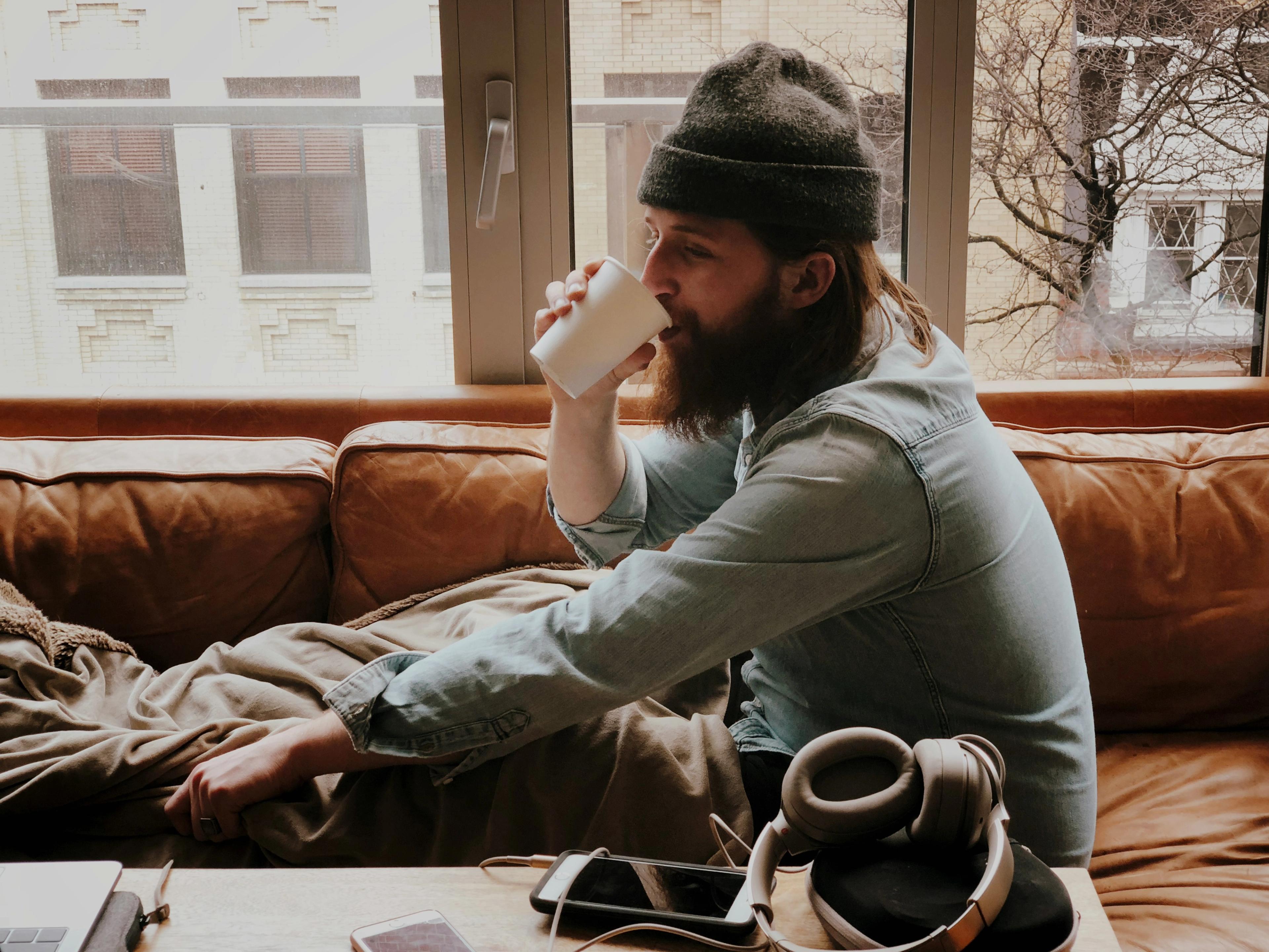 Person sitter på soffa och dricker kaffe.