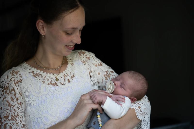 Eine Mutter im weißen Spitzenkleid hält ihr schlafendes Baby im Arm.