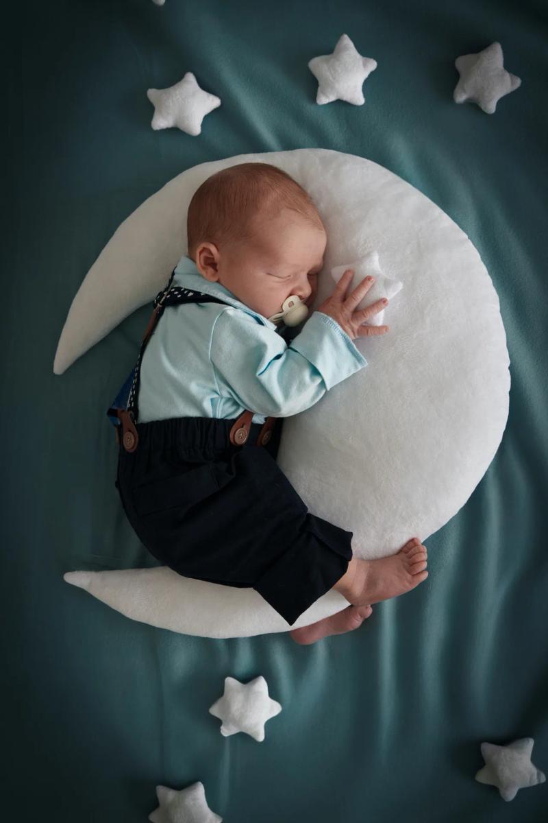 Ein schlafendes Baby liegt auf einem weichen Mondkissen zwischen kleinen Sternen.