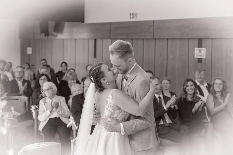 Ein Hochzeitspaar steht während der Trauung vor seinen Gästen, in Schwarz-Weiß.