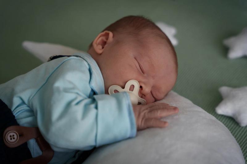 Ein Baby im hellblauen Strampler schläft auf einem hellen Kissen.